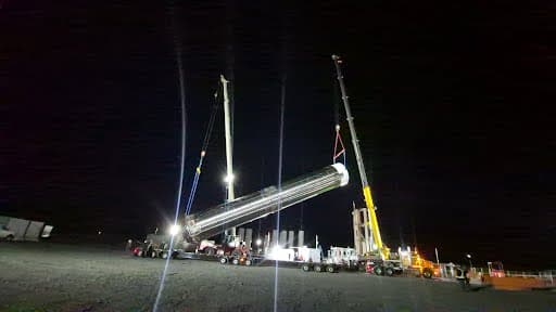 Tandem crane lift upending a long stainless-clad vessel from horizontal to vertical during a night shift