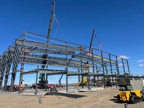 Structural steel staged on site with a telehandler standing by during a commercial building erection