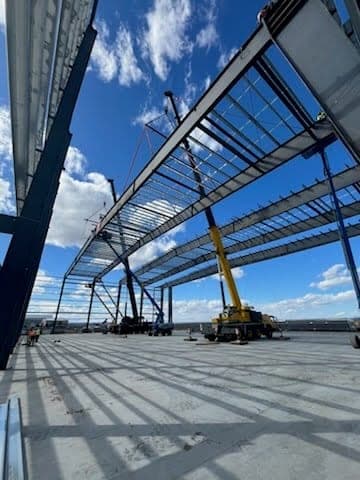 View up through a steel building frame at the crane setting roof framing