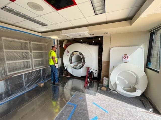 Rigger positioning a medical imaging scanner inside a containment-sealed room during an in-plant equipment move