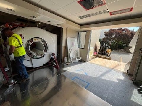 CW Crane & Rigging crew moving a large piece of equipment through a building opening with a forklift during a transload