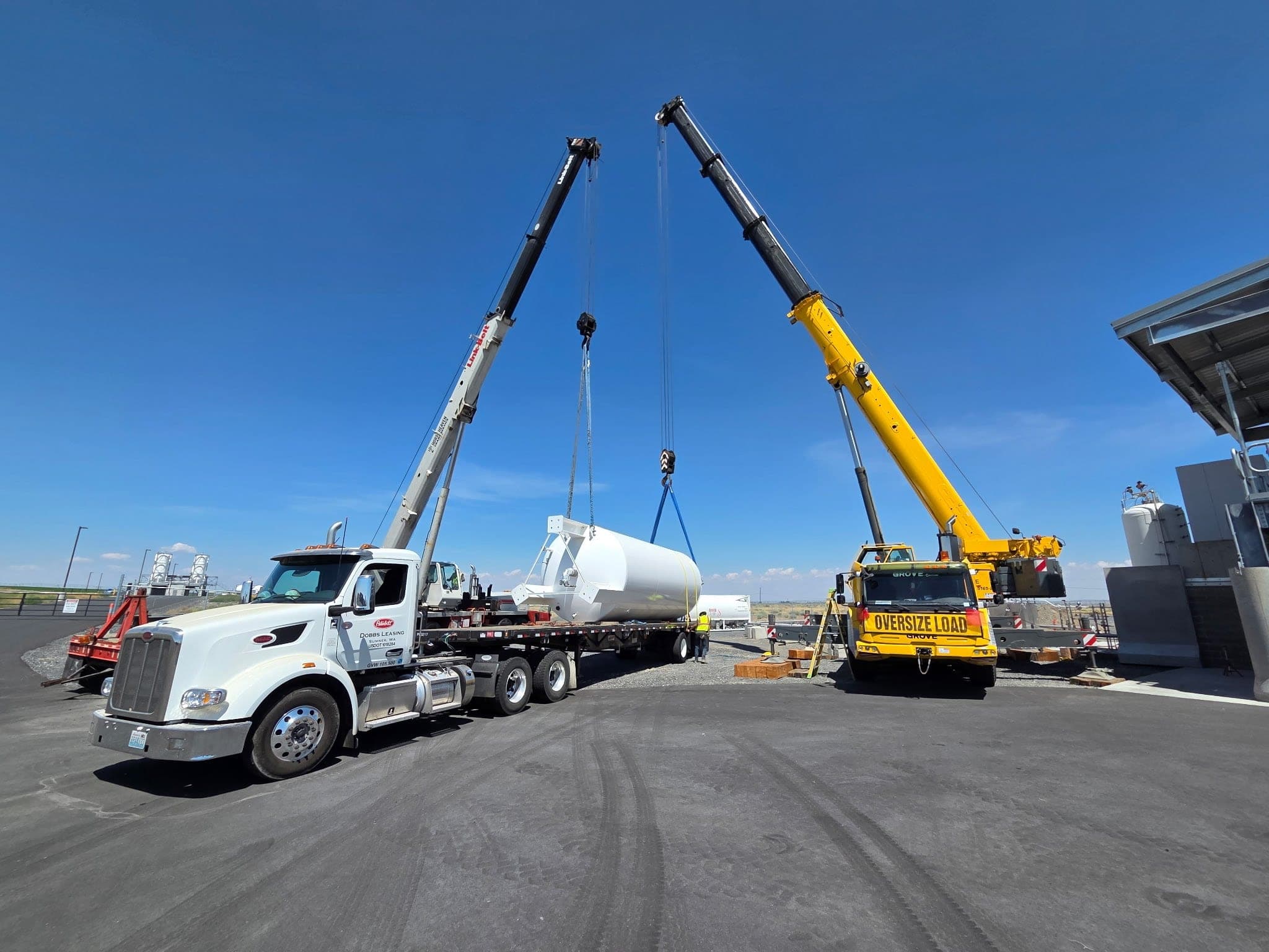 Tandem crane lift removing a large storage tank from a flatbed trailer using multi-point rigging