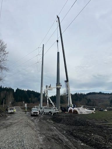 Crane and bucket trucks working together to set a transmission pole on a planned utility lift
