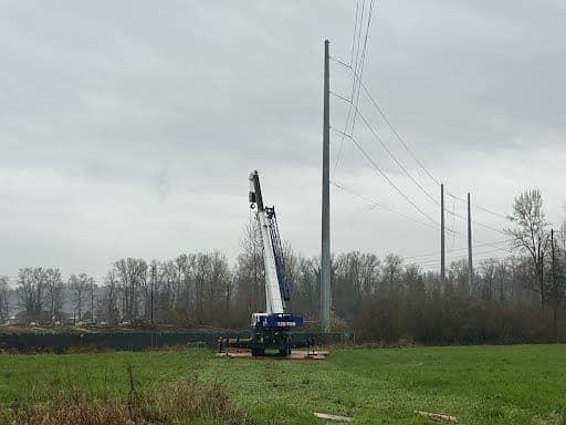 Rough-terrain crane set up in an open field to place a transmission pole in a rural service area